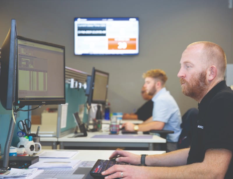 Customer support staff at desks working, tv showing statistics on the wall